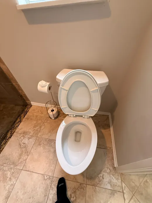 Clean toilet with the lid up in a tan-tiled bathroom