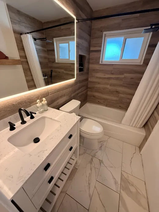 Bathroom with wood-look tile, white vanity and a lit mirror