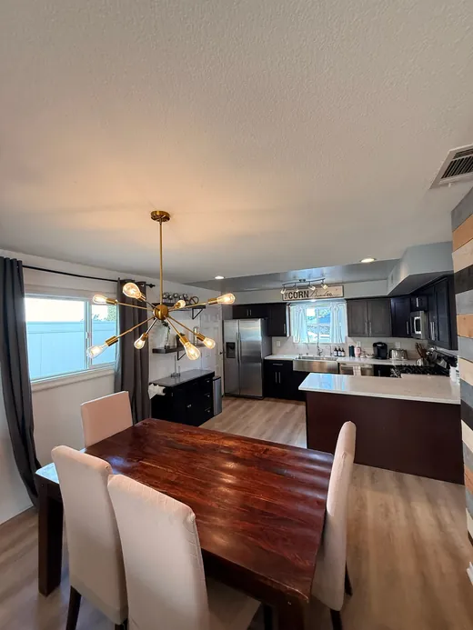 Open dining area and kitchen with dark cabinets and a brass chandelier