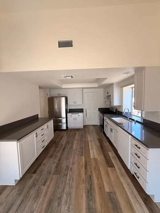 Empty kitchen with white cabinets, gray counters and wood-look floors