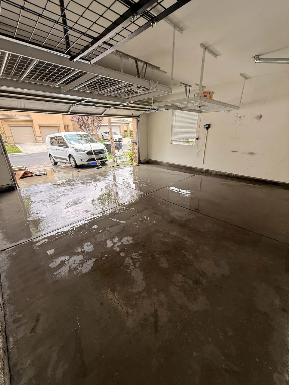 Wet garage floor being washed, with hoses and a surface cleaner