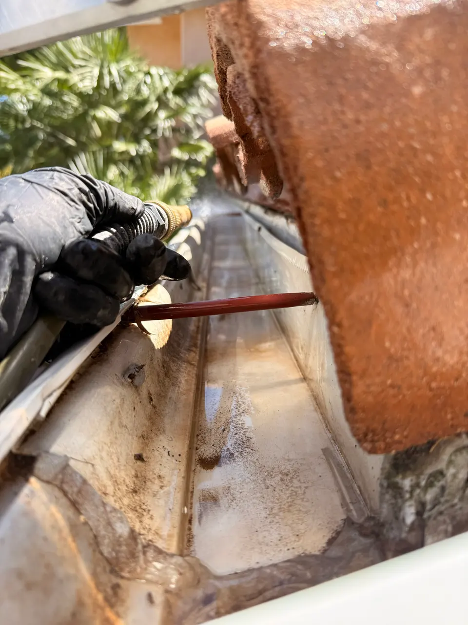 Gloved hand flushing a gutter with a hose