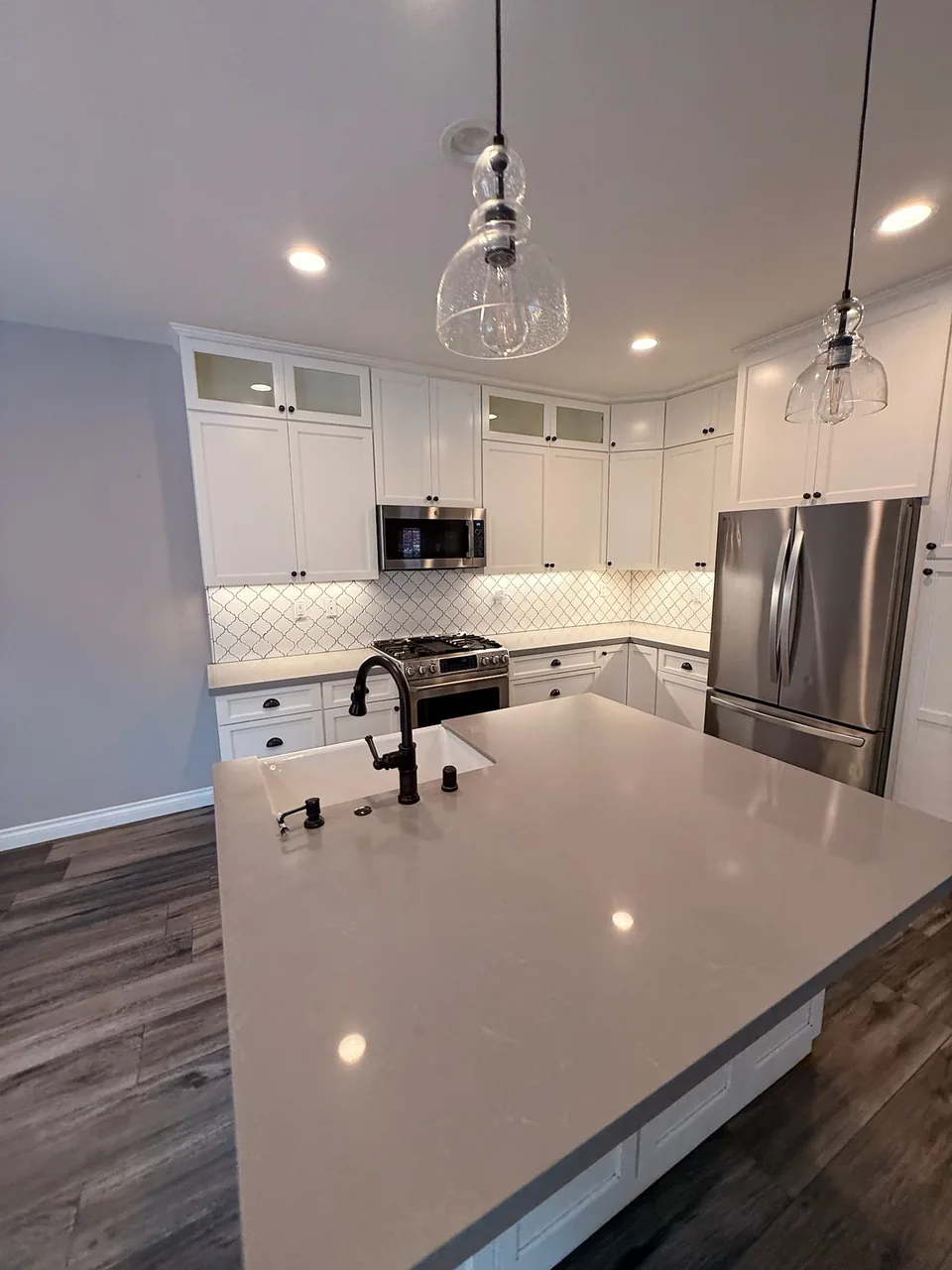 White kitchen with a gray quartz island and pendant lights