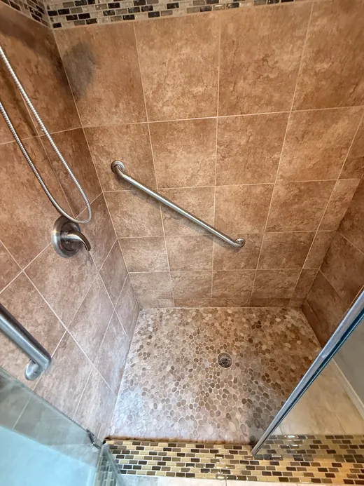 Tiled shower with a pebble floor and grab bar