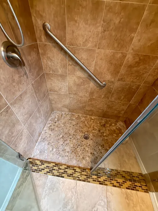 Tiled shower with a pebble floor, grab bar and glass door