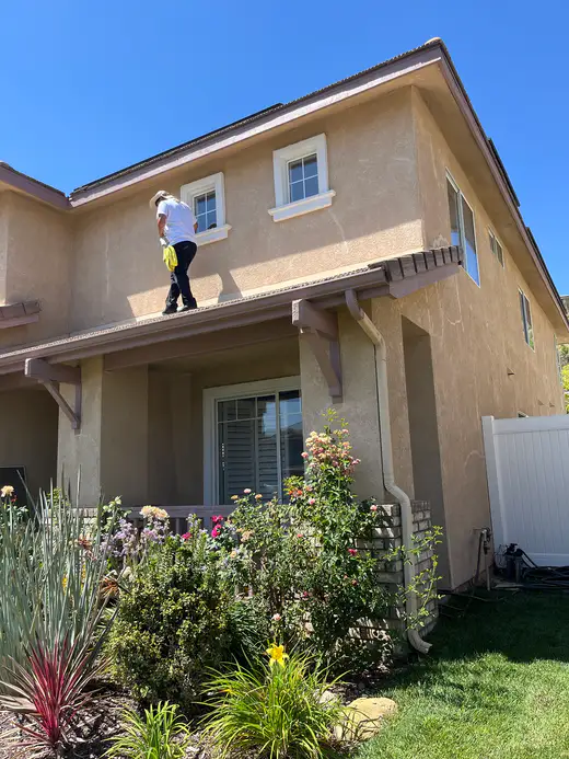 Team member on a porch roof cleaning a second-story window