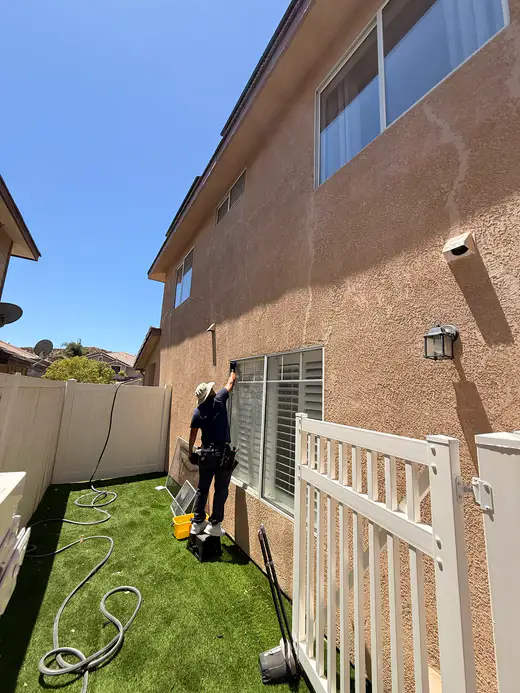 Team member on a step stool cleaning a window in a side yard